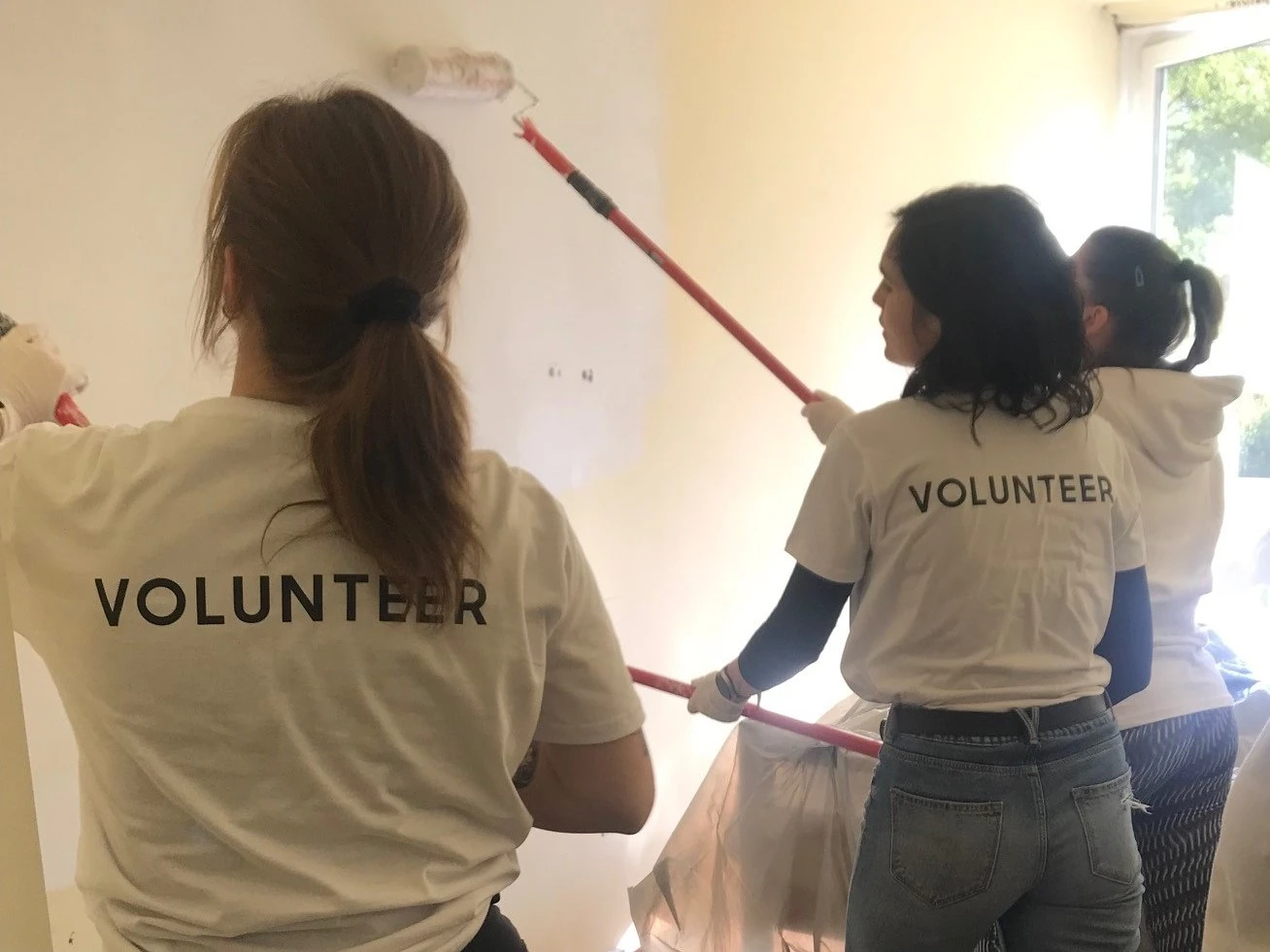 Önkéntesek festenek ki egy szobát, a pólójukon VOLUNTEER felirat