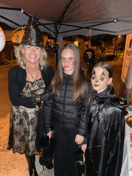 Egy boszorkánynak öltözött felnőtt két beöltözött, kifestett arcú gyerekkel