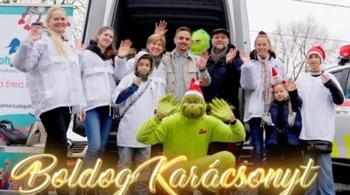 Az alapítvány önkéntesei és gyerekek egy Grincs-jelmezes figurával, Boldog Karácsonyt felirattal